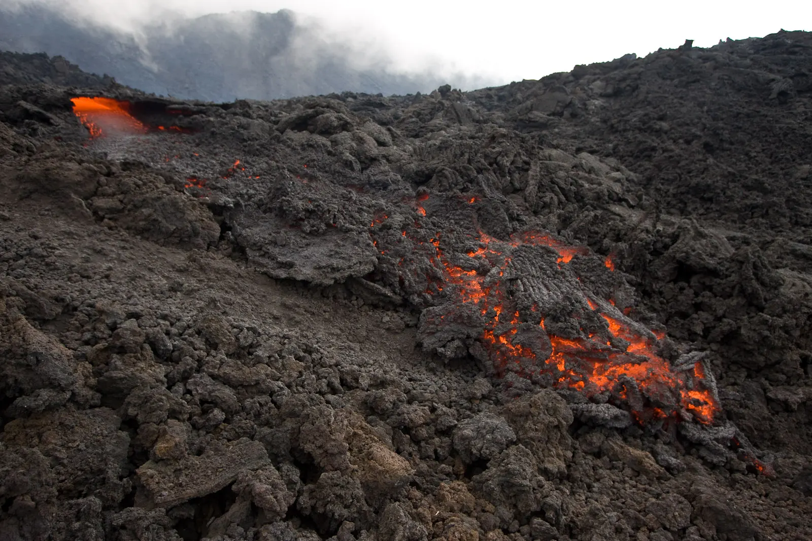 Hikers crossing a black lava field below the cone of Pacaya volcano, Antigua, Guatemala