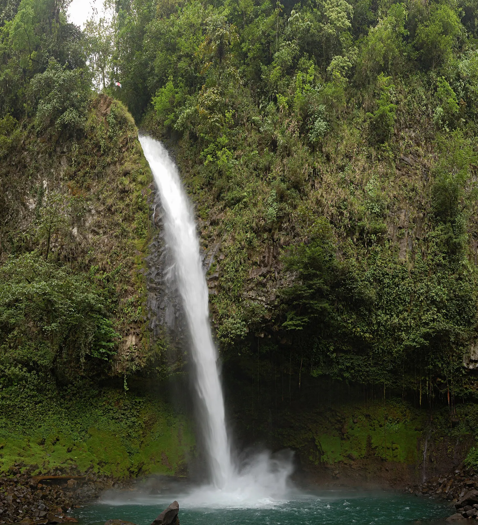 A tall waterfall plunging into a green pool surrounded by rainforest, Arenal, Costa Rica