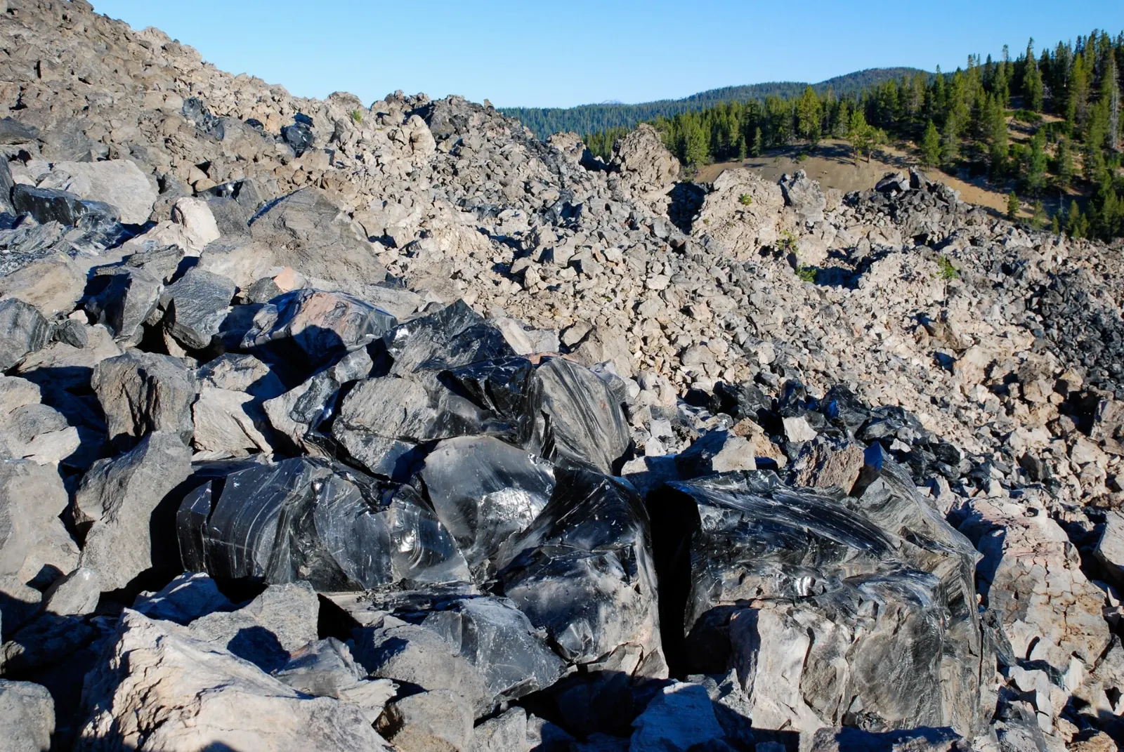 Black glassy obsidian rock of the Big Obsidian Flow under a blue sky, Bend, Oregon