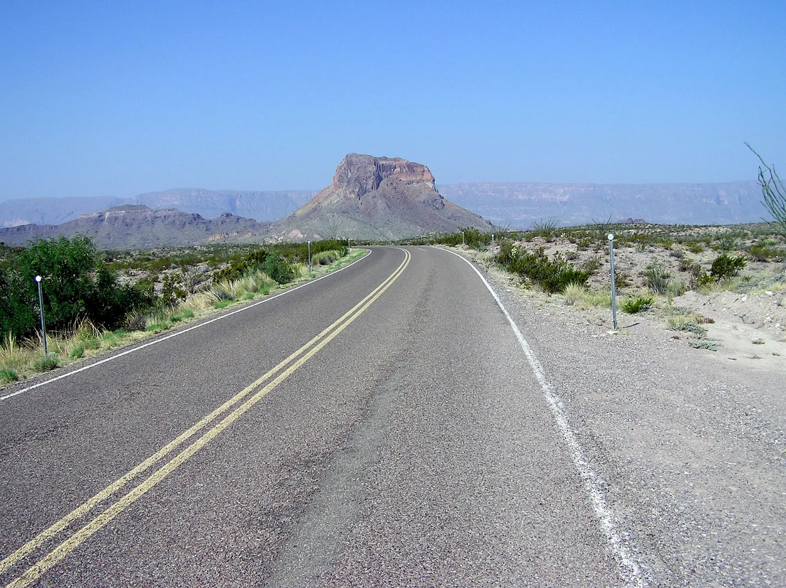 Paved road winding through colorful desert hills toward distant mountains in Big Bend, Big Bend National Park, Texas