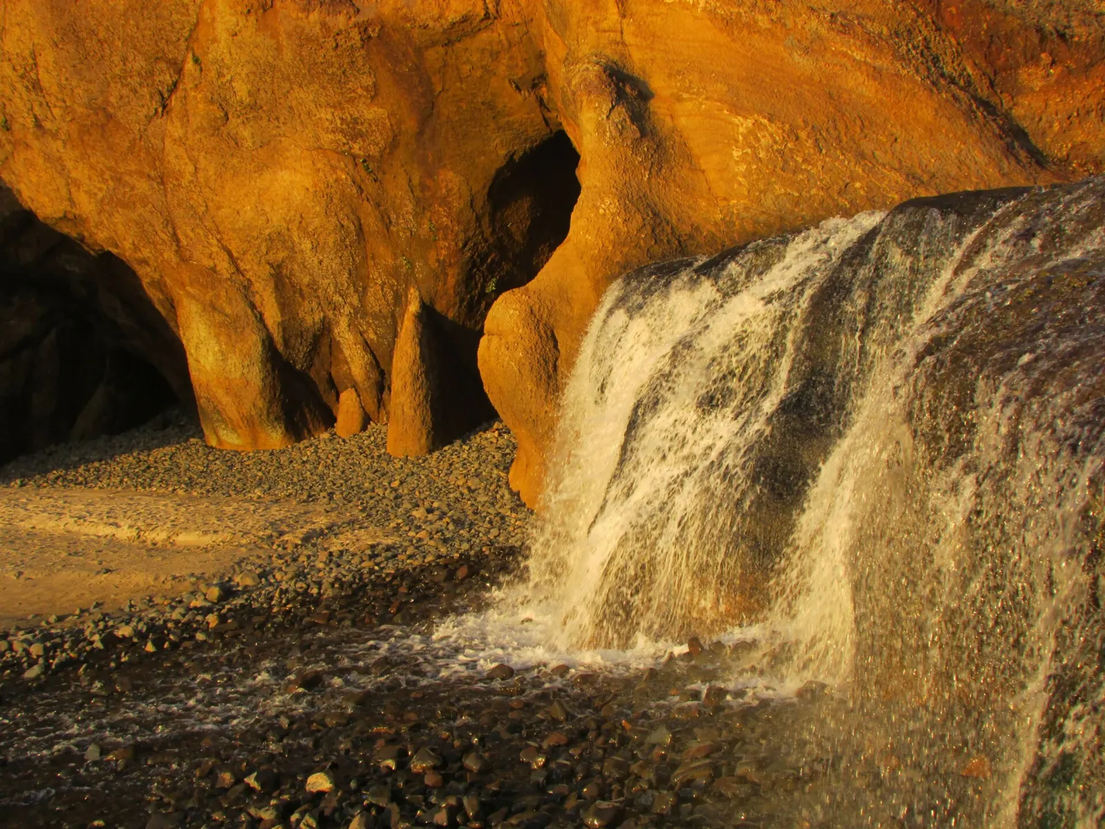 Fall Creek waterfall pouring onto the beach at Hug Point beside sandstone cliffs, Cannon Beach, Oregon