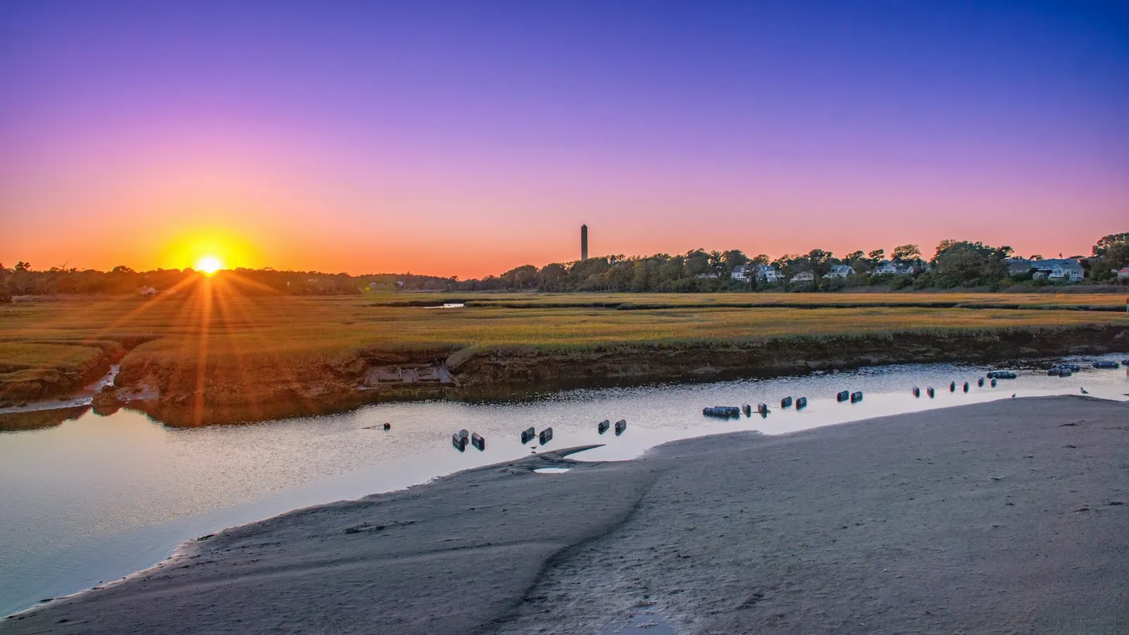 A long wooden boardwalk crossing green salt marsh toward the dunes in Sandwich, Cape Cod, Massachusetts