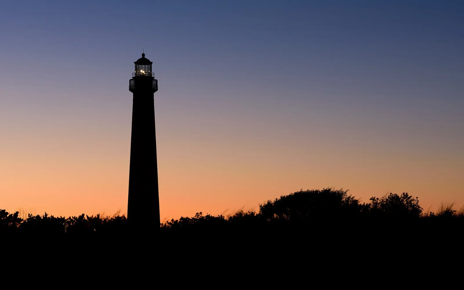 The tall cream-colored Cape May Lighthouse with a red top above dunes and trees, New Jersey