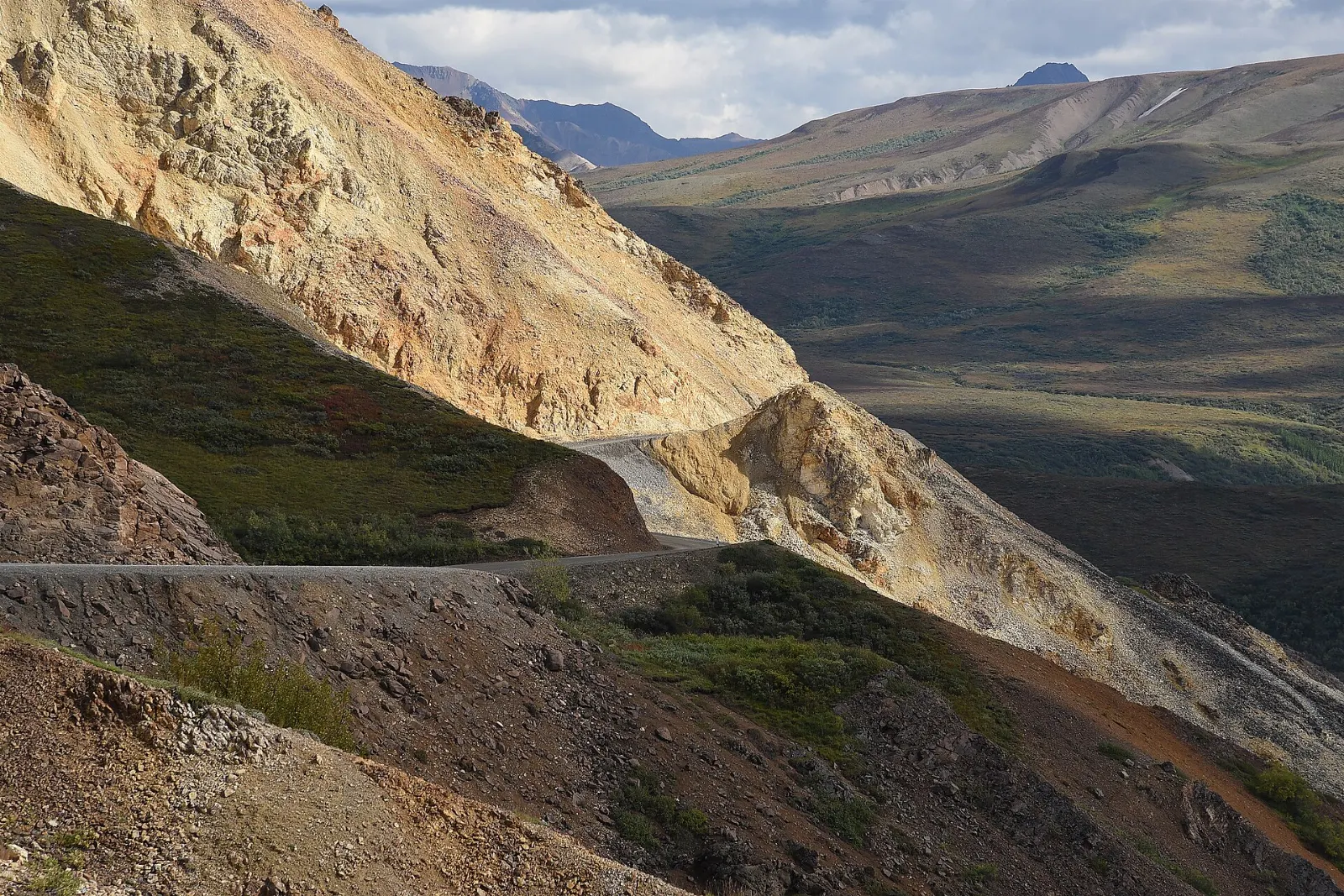 Multicolored volcanic bluffs and a winding gravel road high above a wide valley, Denali National Park, Alaska