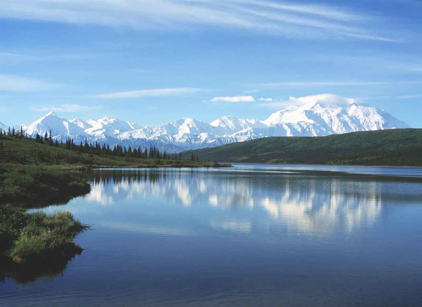 A calm lake reflecting a massive snowy mountain under a clear sky, Denali National Park, Alaska