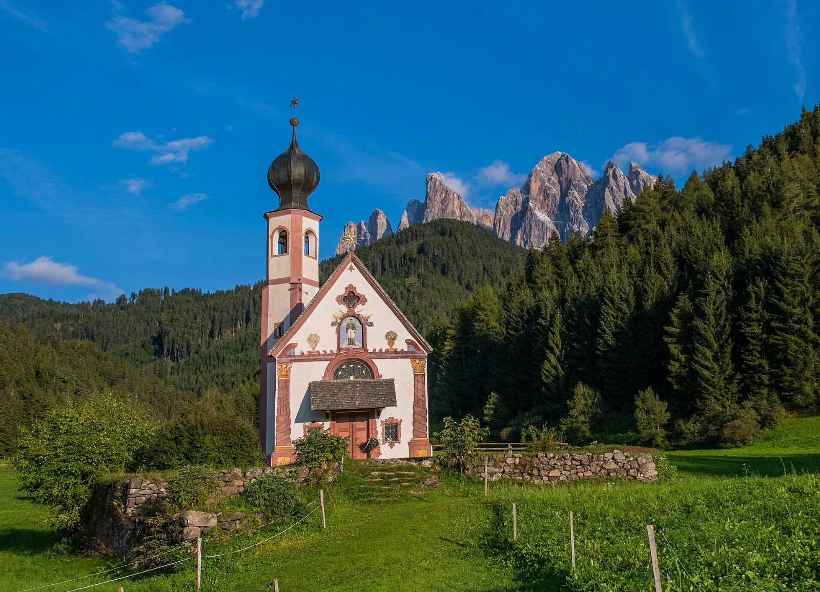A small baroque chapel in a meadow beneath the jagged Odle peaks, Dolomites, Italy