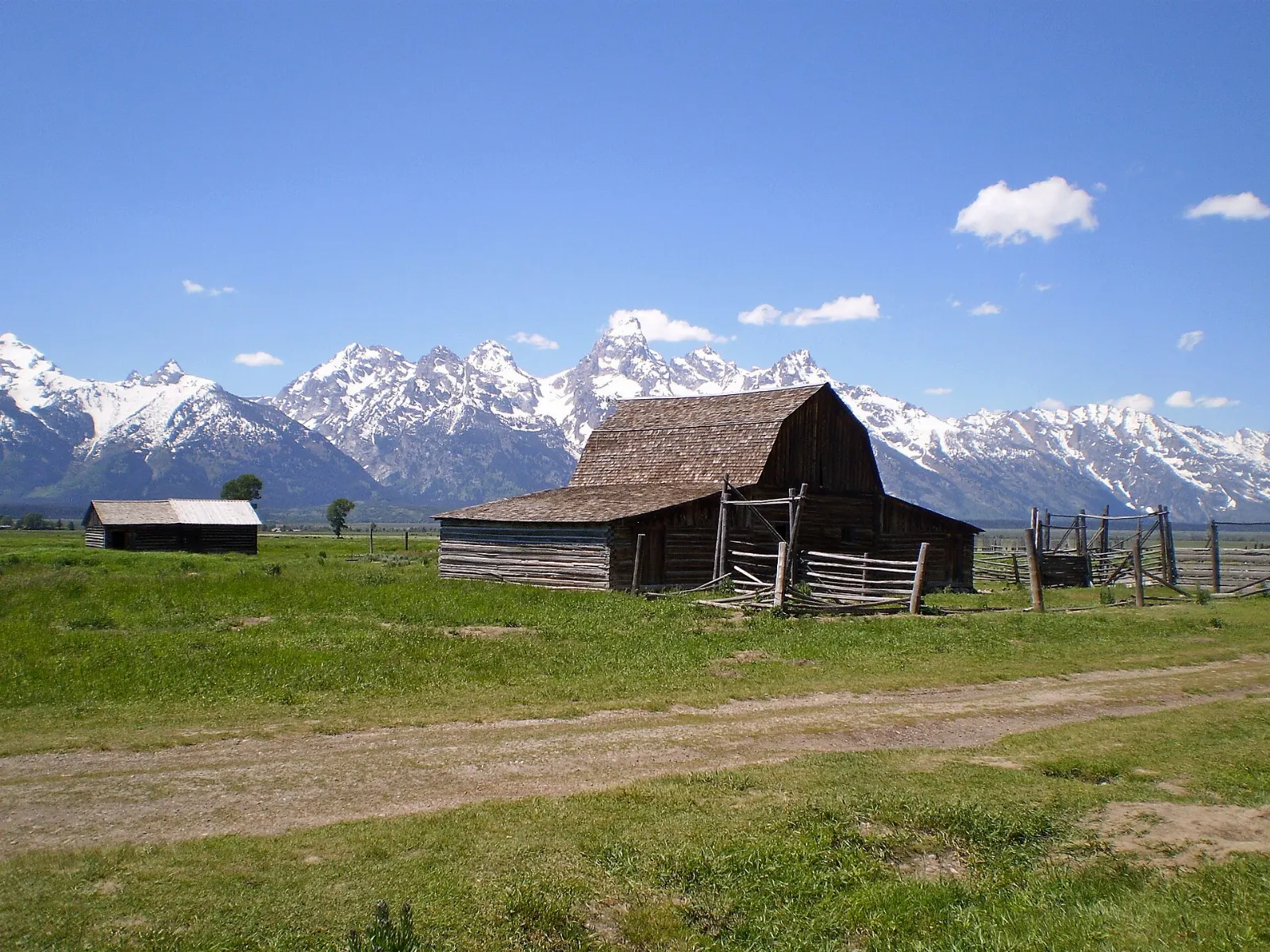 A weathered wooden barn with a pitched roof standing on sagebrush flats beneath the Tetons, Grand Teton National Park, Wyoming