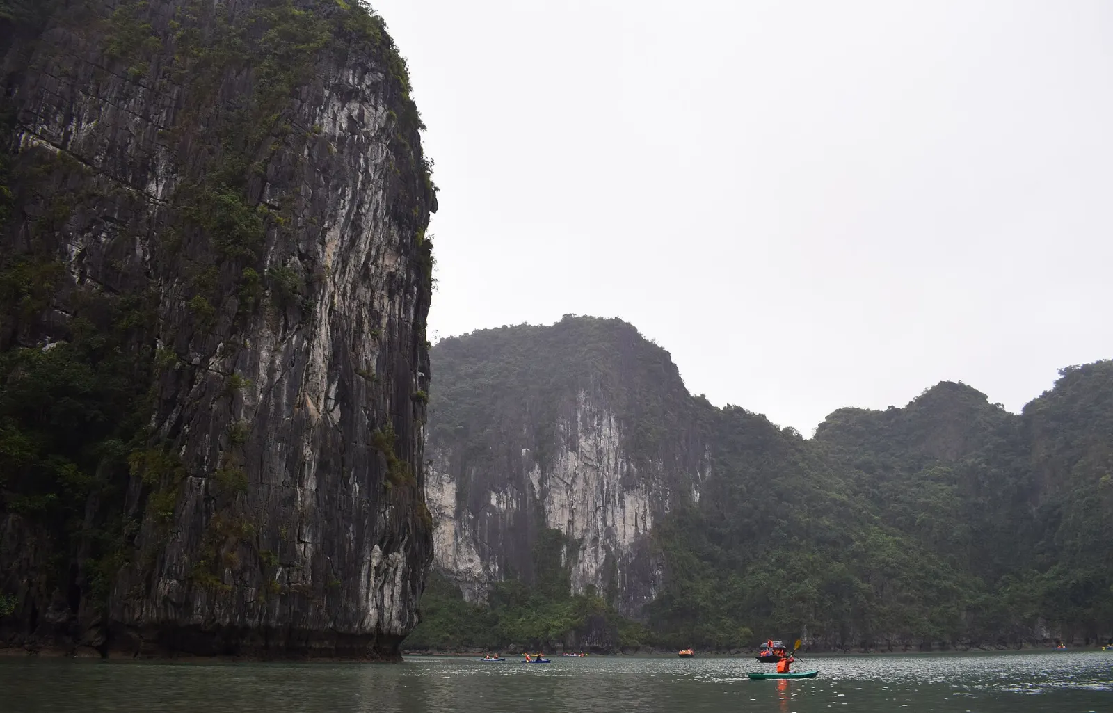 Kayaks and bamboo boats passing under the low arch of Luon Cave into an enclosed lagoon, Ha Long Bay, Vietnam
