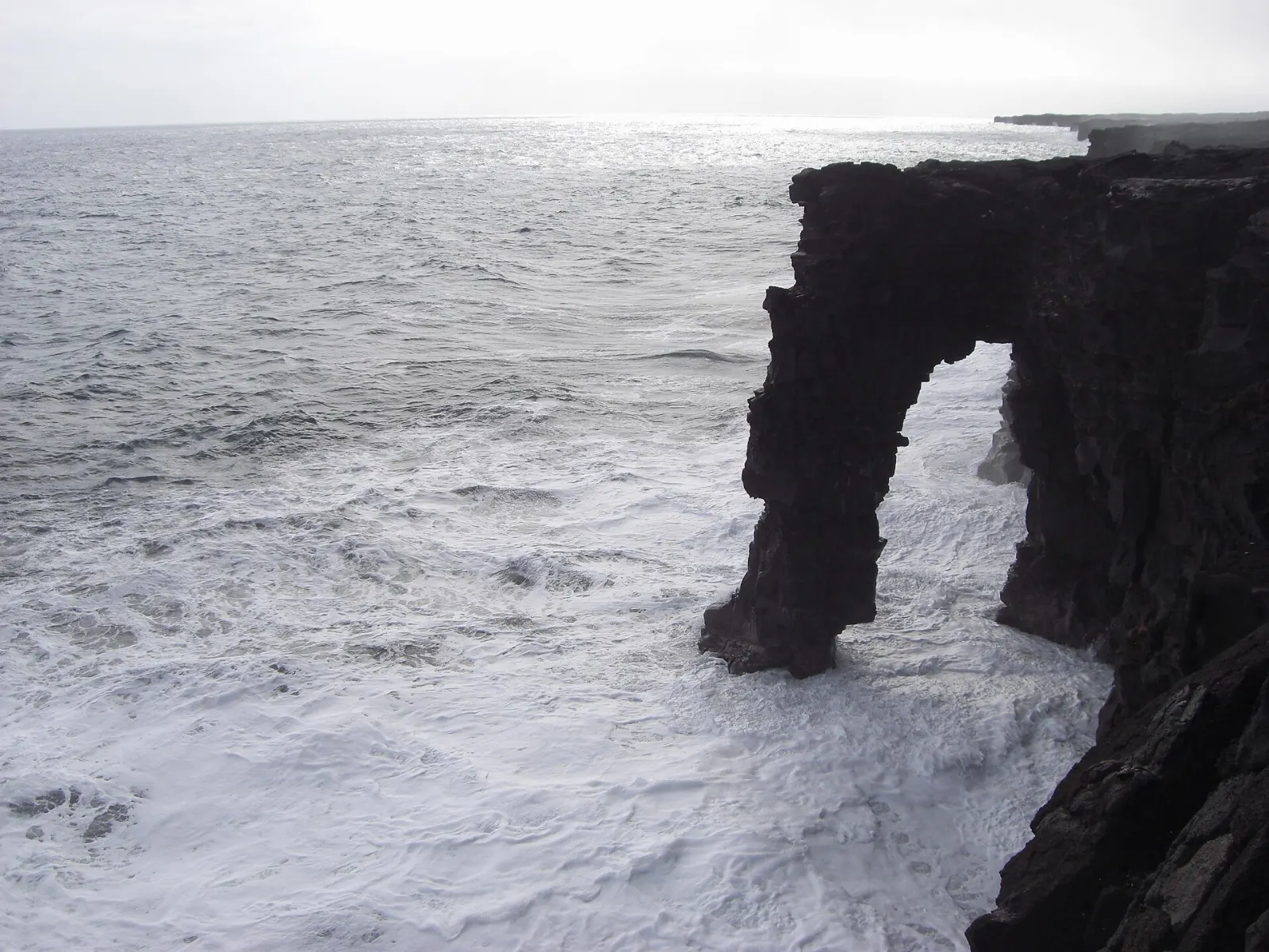 A lava rock sea arch standing above crashing waves on the park's southern coast, Hawaii Volcanoes National Park, Hawaii