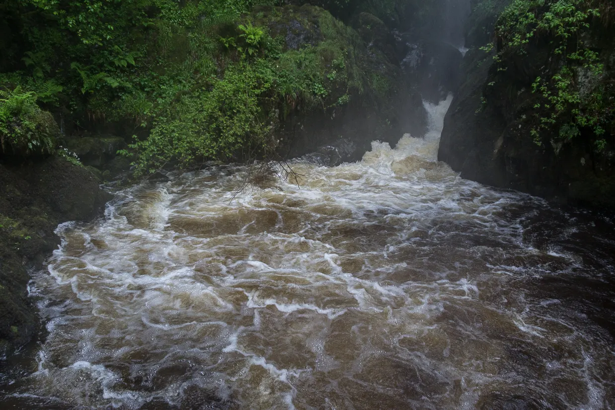 A waterfall dropping beneath a stone footbridge in a wooded ravine above Ullswater, Lake District, England