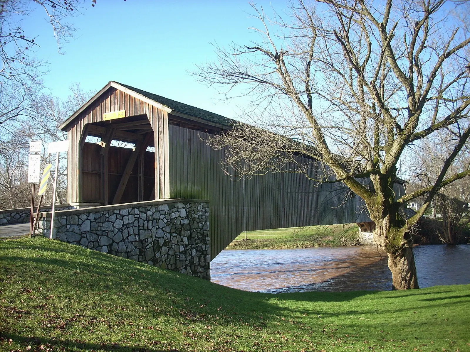 A red wooden covered bridge spanning the Conestoga River among trees, Lancaster County, Pennsylvania