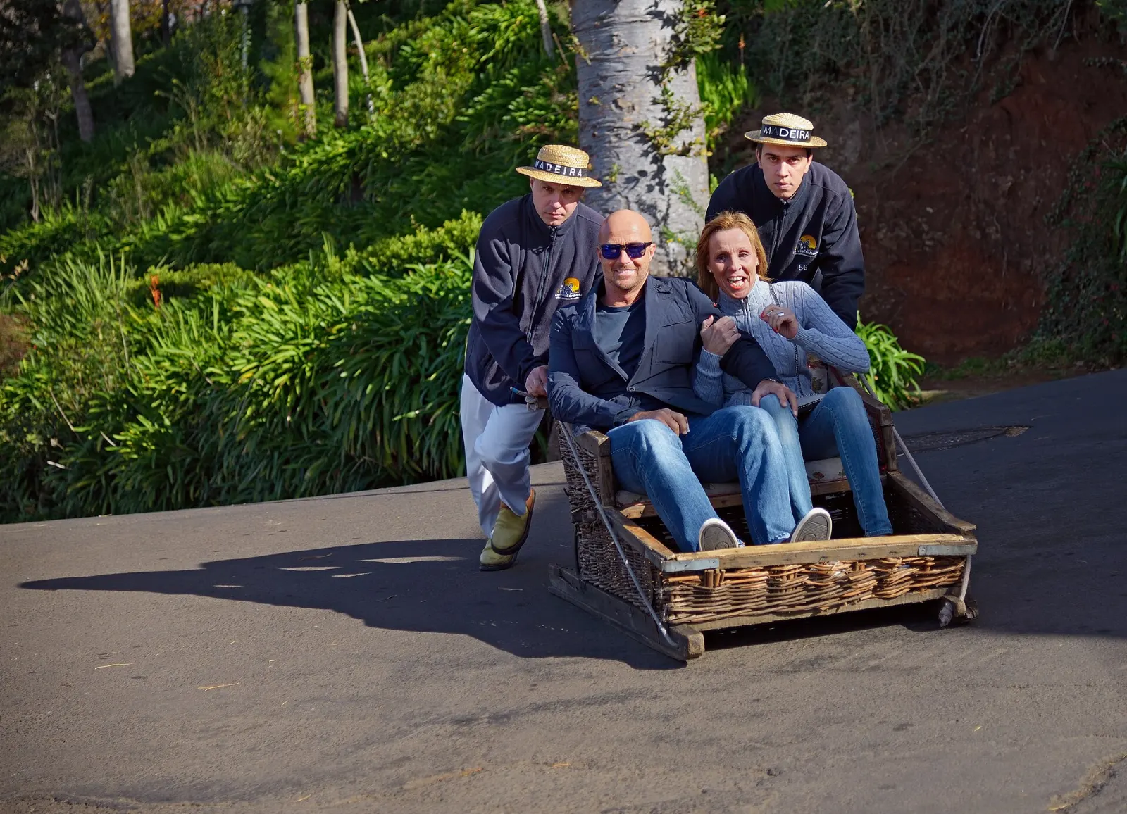 Two drivers in white steering a wicker toboggan down a steep street in Monte, Madeira, Portugal