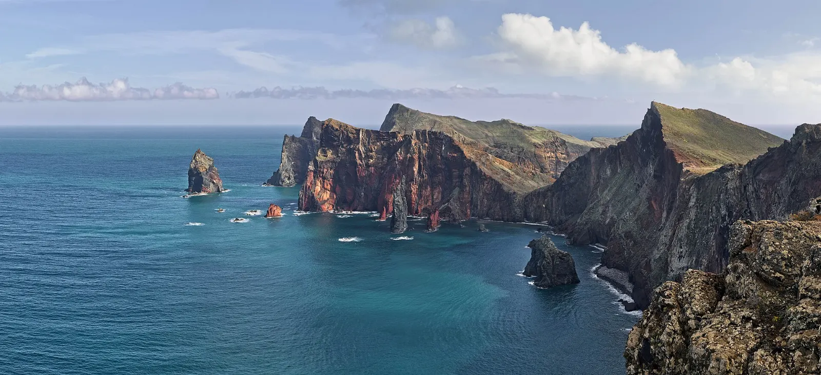 A narrow, rugged peninsula of reddish and ochre cliffs reaching into the sea, Madeira, Portugal