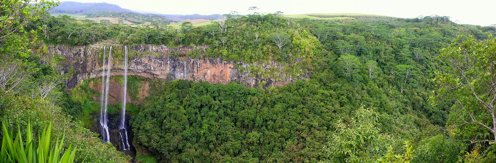 A tall waterfall dropping over a basalt cliff into a green gorge near Chamarel, Mauritius