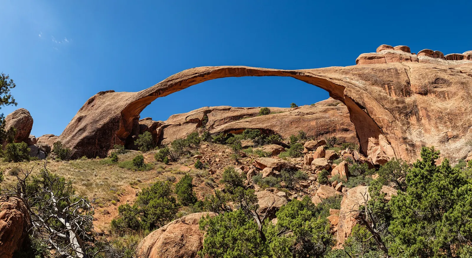 The long, thin ribbon of Landscape Arch spanning a sandy wash, Moab, Utah