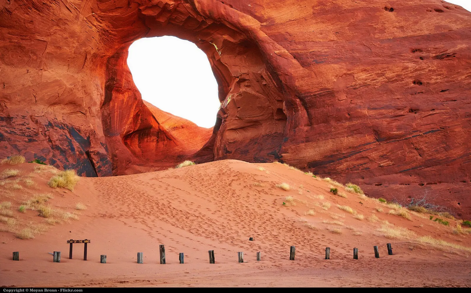 A large natural arch opening in a sandstone wall above red sand dunes, Monument Valley, Arizona and Utah