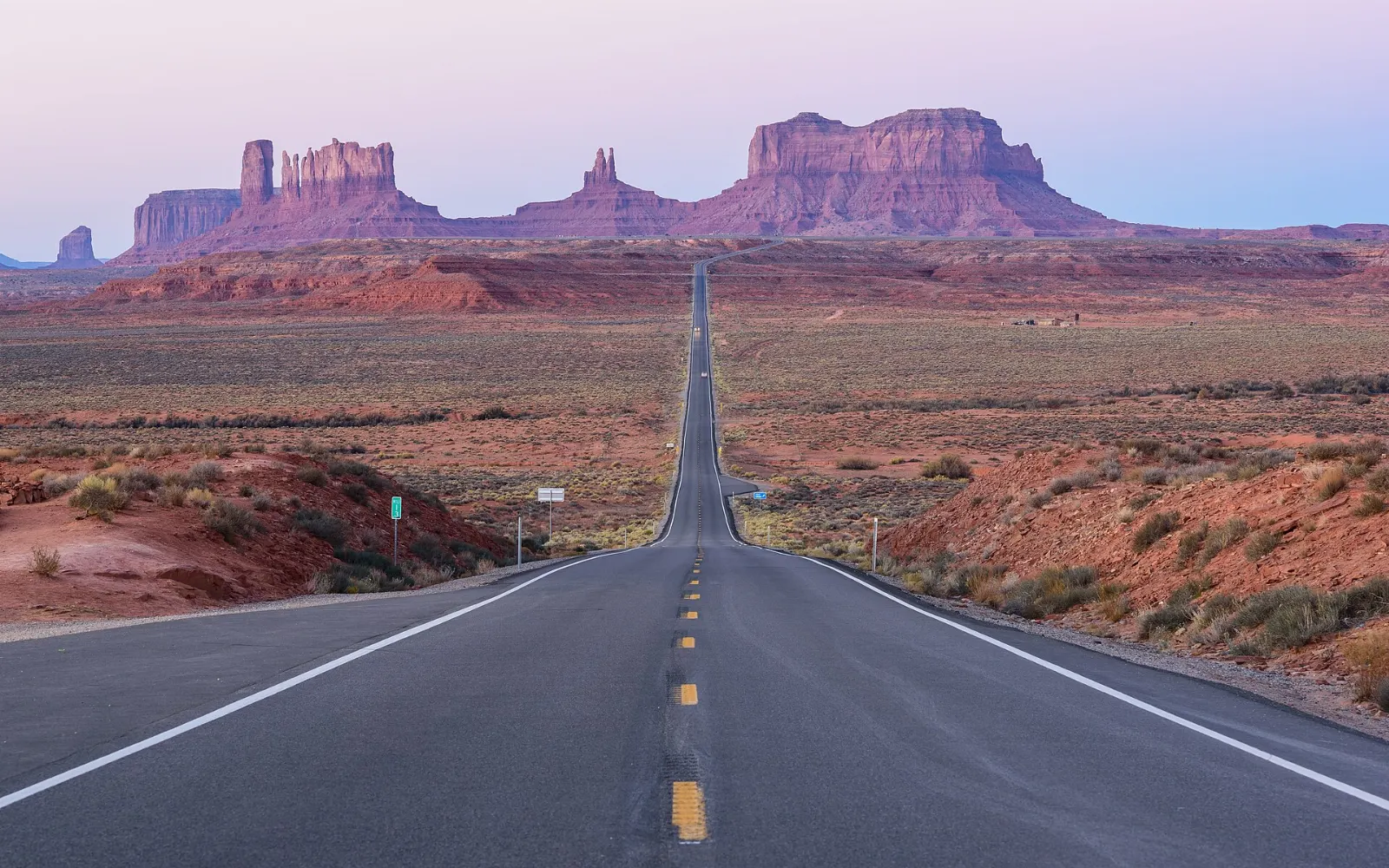 A straight two-lane highway leading toward the distant buttes of Monument Valley