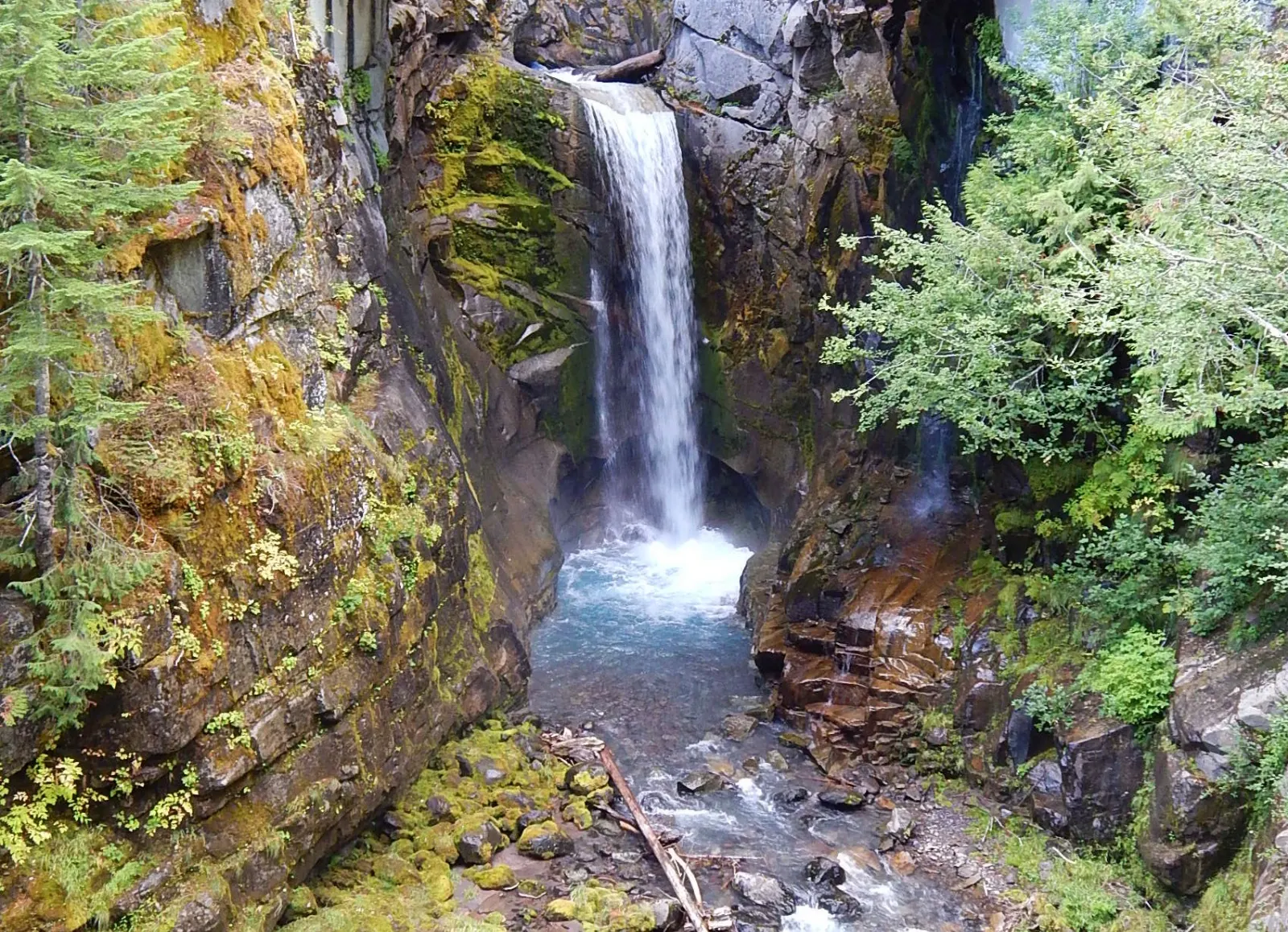 Waterfall framed by the stone arch of a road bridge in a mossy gorge, Mount Rainier National Park, Washington