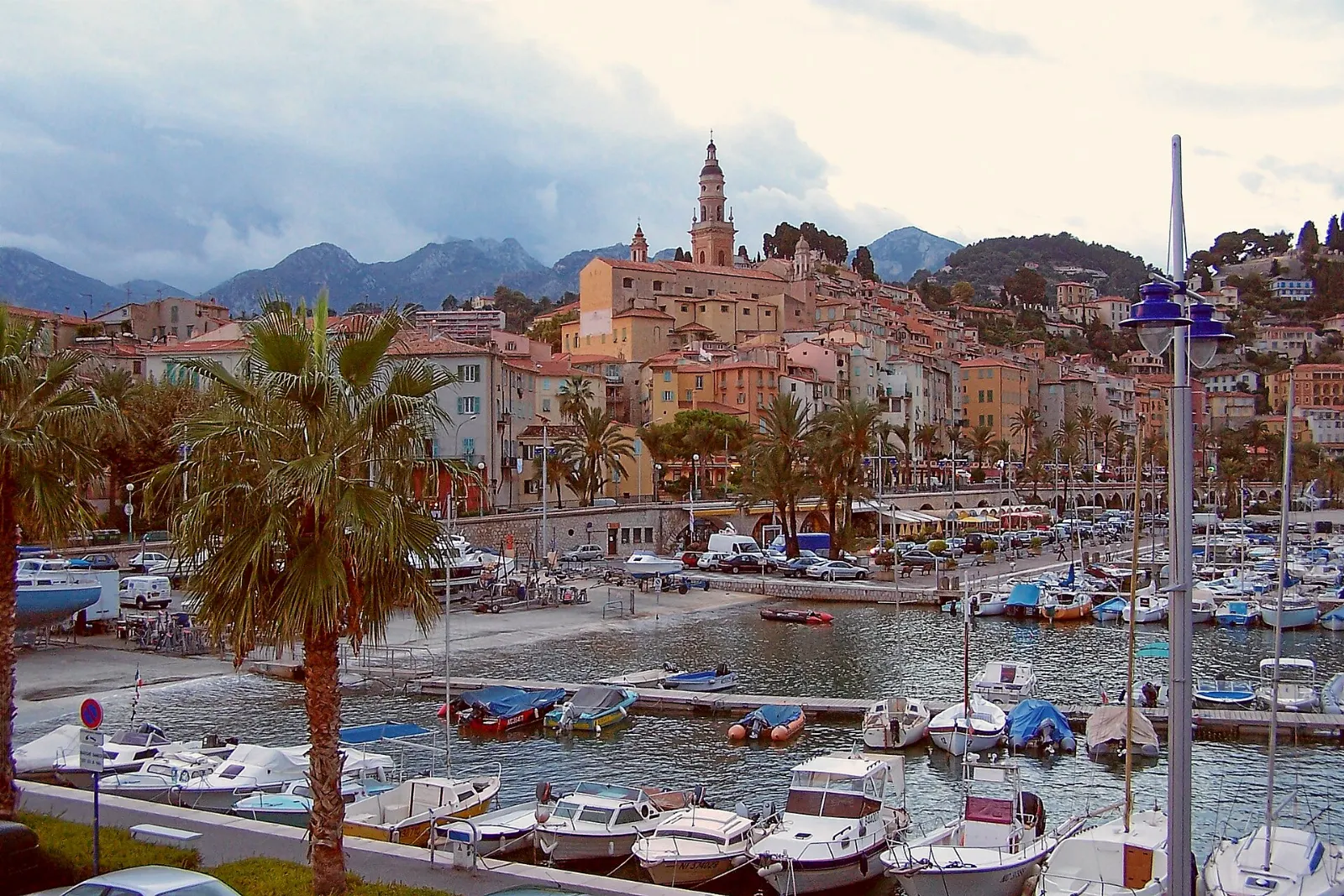 Colorful houses of Menton's old town rising up a hill behind the beach, topped by a basilica, Nice and the French Riviera, France