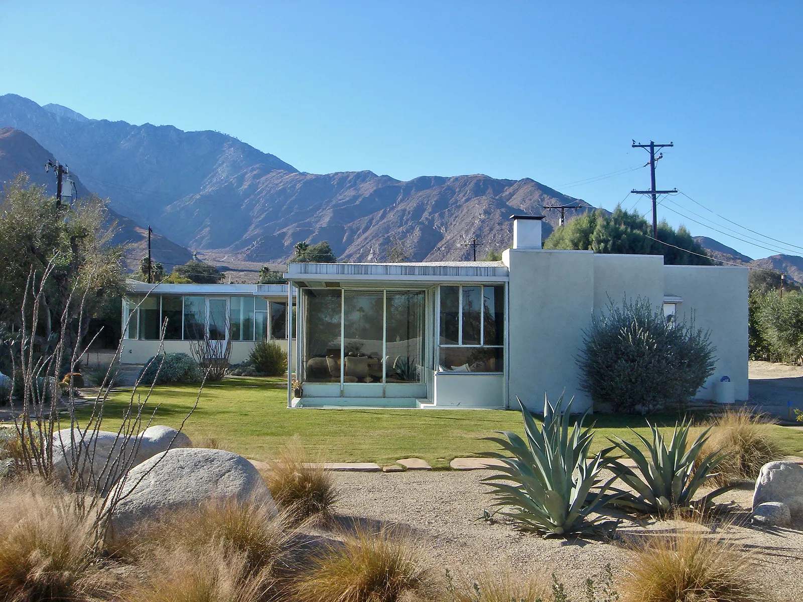A low glass and steel modernist house with a lawn and mountain backdrop, Palm Springs, California