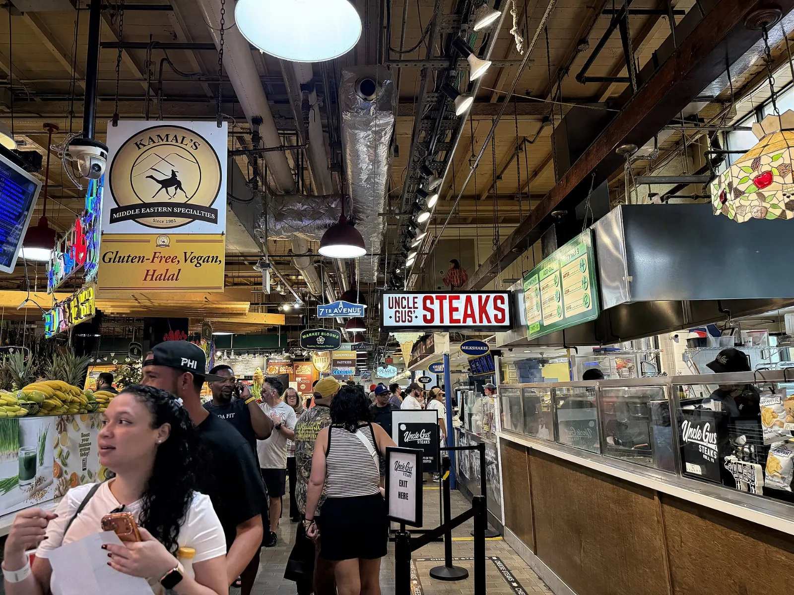 Shoppers walking between food stalls under signs inside Reading Terminal Market, Philadelphia, Pennsylvania
