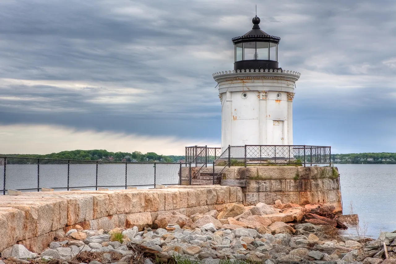 Small white Portland Breakwater Light with classical columns at the end of a grassy point, Maine