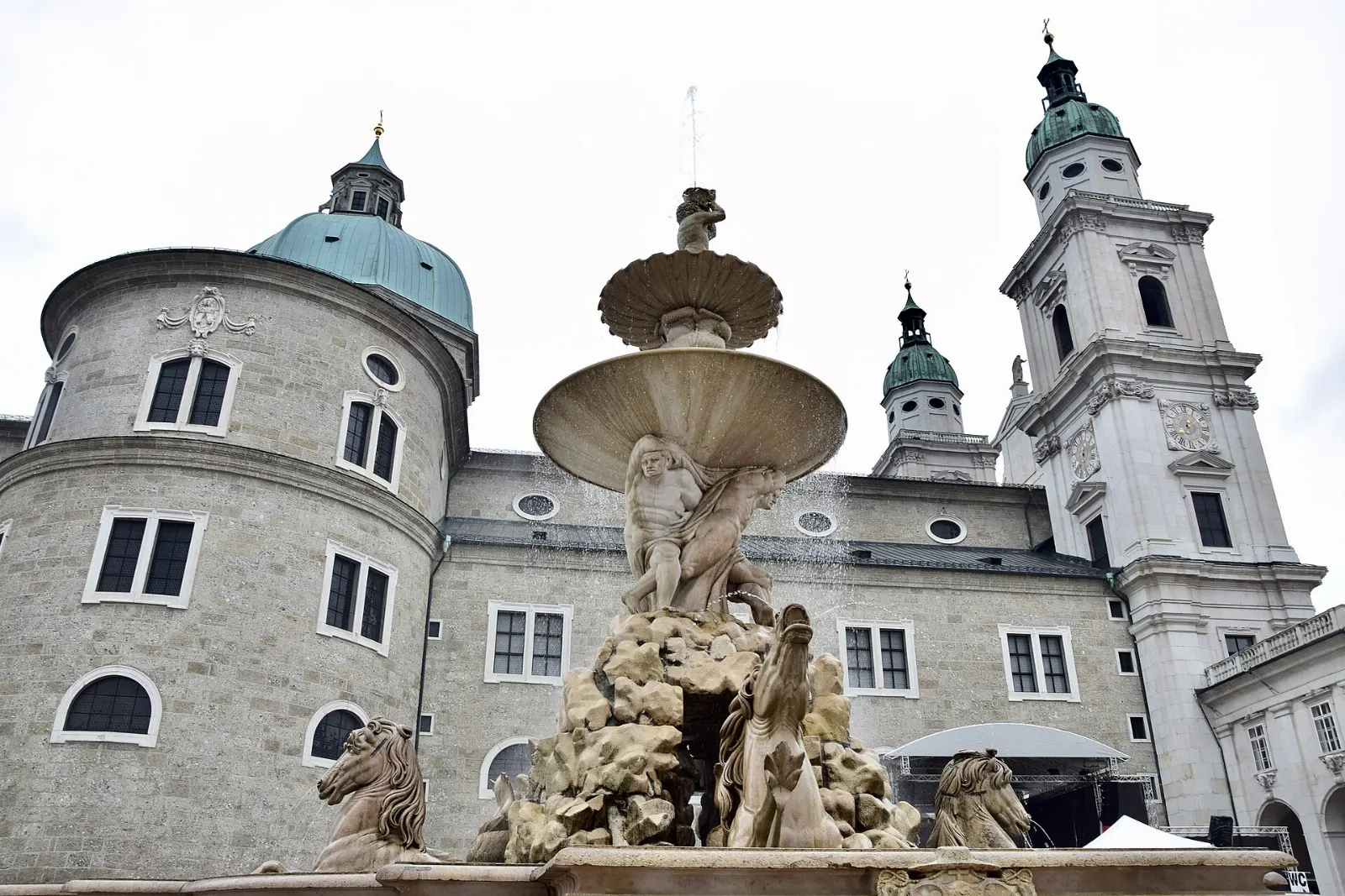 A large Baroque fountain with horses and figures in a wide square beside palace buildings, Salzburg, Austria