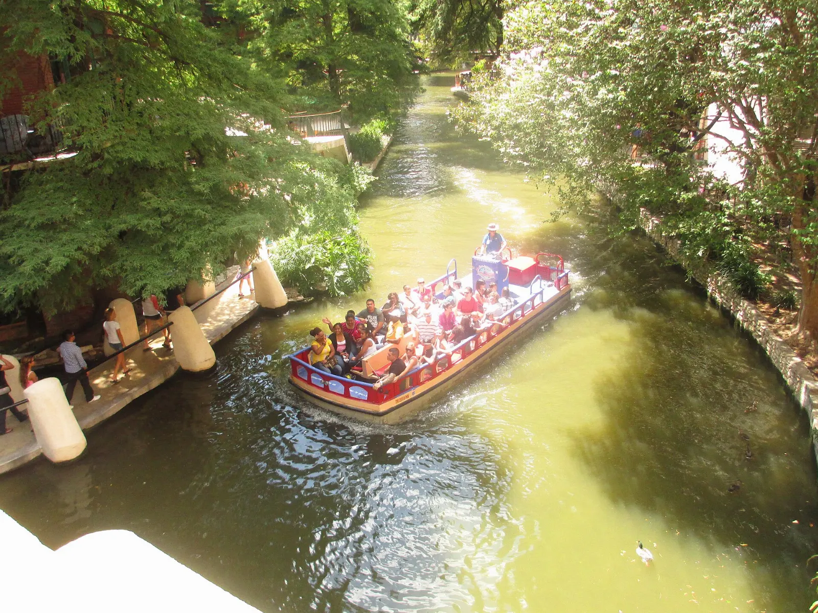 Open river barge full of passengers passing under a stone bridge on the River Walk, San Antonio, Texas