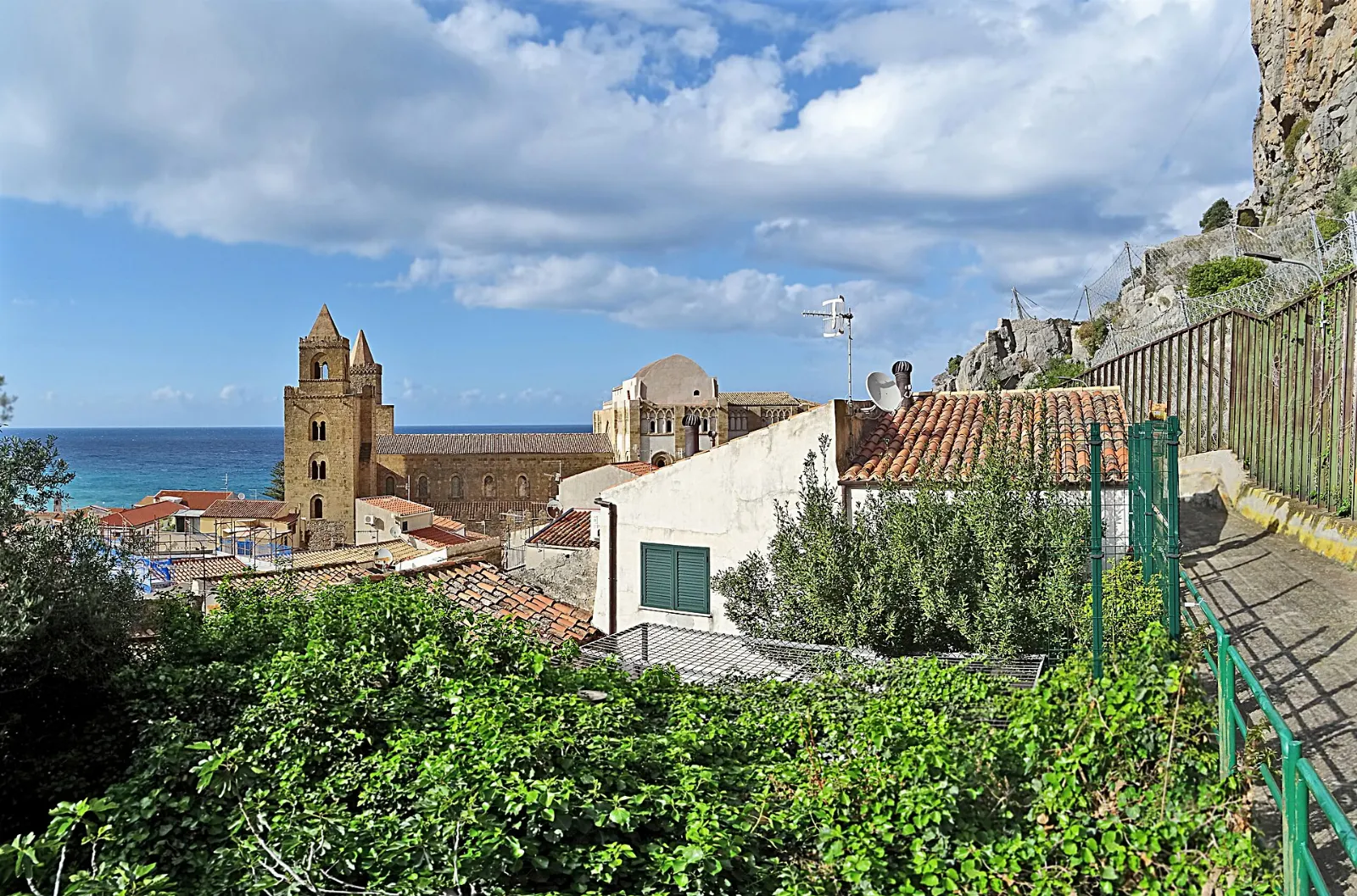A Norman cathedral with twin towers beneath a massive rocky headland, Sicily, Italy