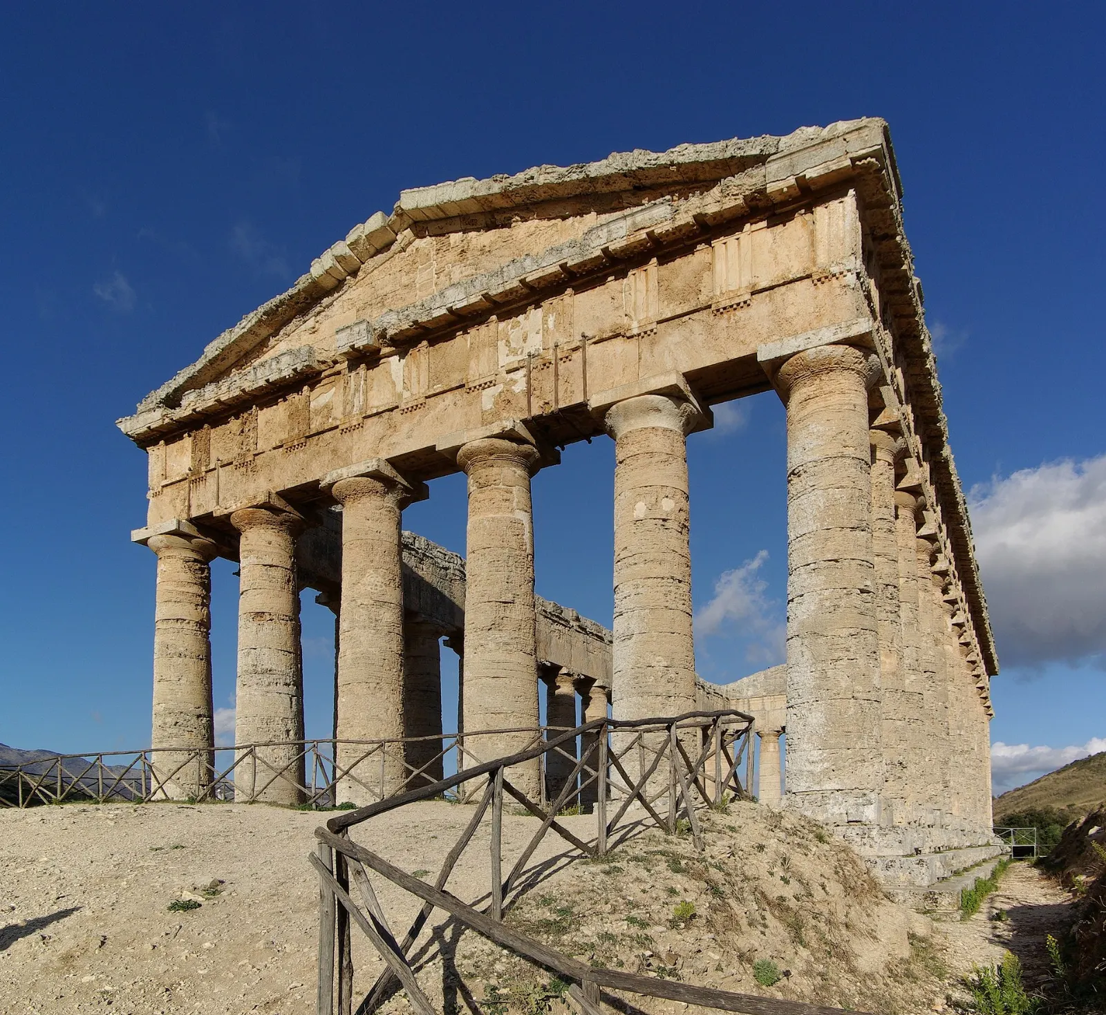 A Doric temple with intact columns standing alone on a green hillside, Sicily, Italy