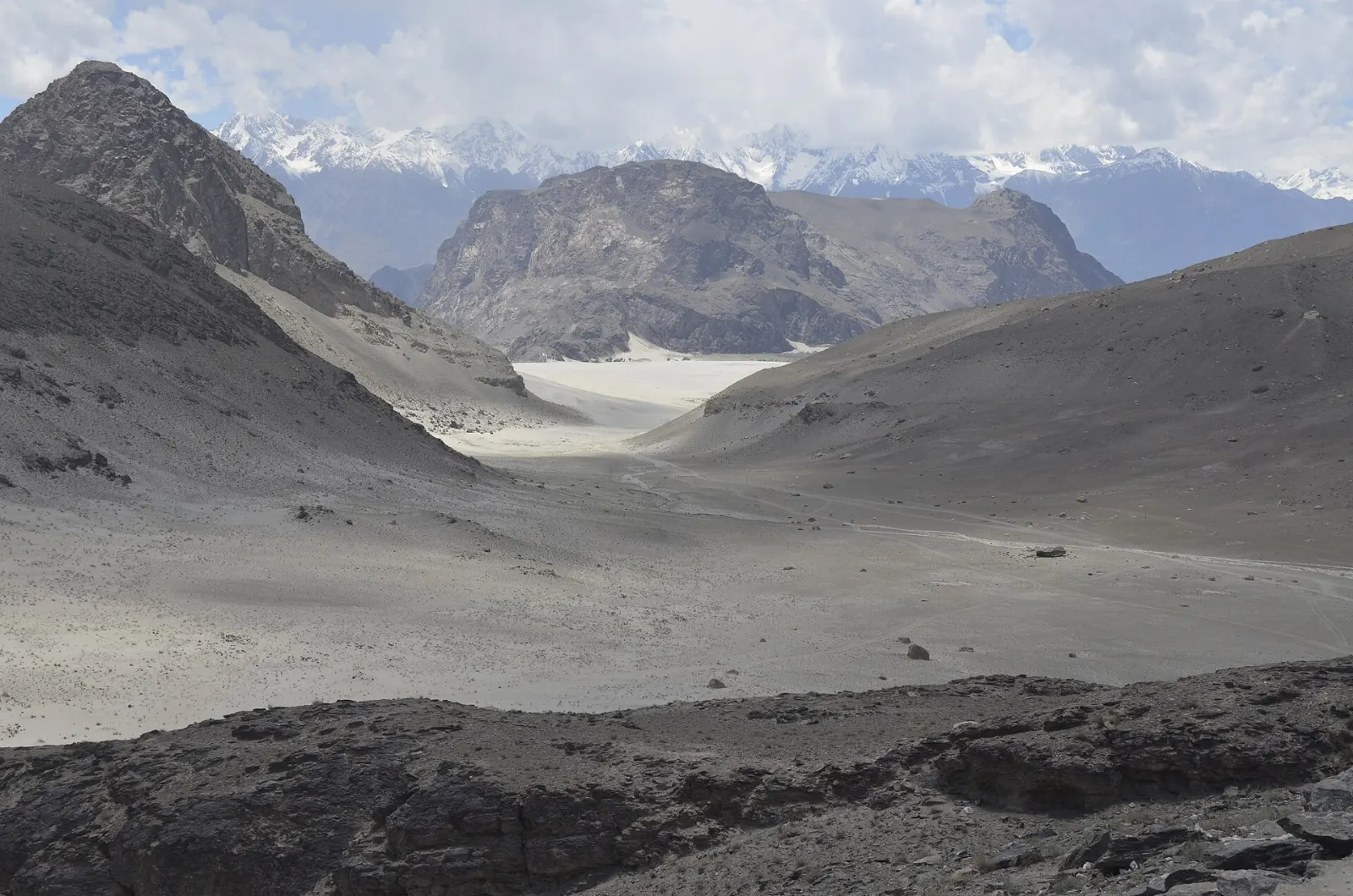 Pale sand dunes of a high-altitude cold desert beneath rocky mountains in Baltistan, Skardu, Pakistan