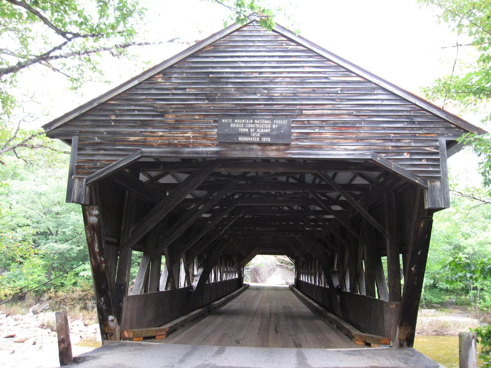A red wooden covered bridge spanning the Swift River surrounded by trees, White Mountains, New Hampshire